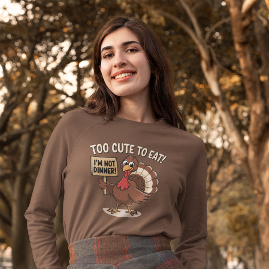 'Too Cute to Eat!' t-shirt from Trippy Outfitters featuring an adorable cartoon turkey with big, sparkling eyes and a cheeky smile, holding a sign that reads 'I’m not dinner!' in a whimsical font. This delightful design is perfect for spreading holiday cheer with humor and good vibes. Soft and comfortable, this tee adds fun to any outfit, making it a festive choice for feasts or cozy days.